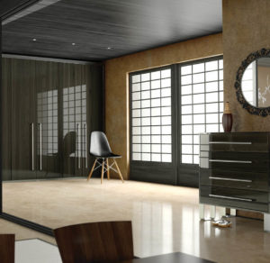 A minimalist interior with a modern chair, polished floor, and large windows featuring grid-patterned shades. A sleek dark dresser stands to the right, topped with a vase and decor, under a circular wall mirror. The space is illuminated by natural light.