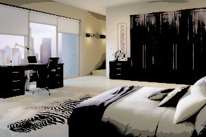 Modern bedroom and office space with a city view. Features a large bed with neutral bedding, a zebra-patterned rug, a wooden desk with a computer and chair, and a wardrobe. Natural light streams through large windows, highlighting the minimalist decor.