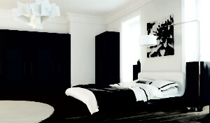 A modern bedroom with a low, white bed featuring white and dark gray bedding. The room has dark gray wardrobes along one wall, a round rug on the wooden floor, a large flower artwork above the bed, and a unique geometric ceiling light.