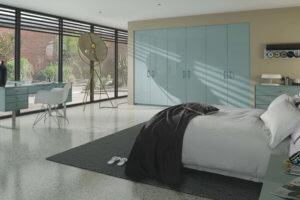 A modern bedroom featuring a large frosted glass wardrobe and a unique tripod floor lamp. The room has a minimalist design with abundant natural light streaming through the large windows. A bed with dark bedding is partially visible.