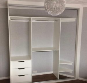 A minimalist walk-in closet with white shelving and drawers. Several sections for organizing clothes, including hanging rods and open shelves. A modern, spherical light fixture hangs above.