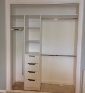 An open closet with white shelving and drawers on the left side, and two hanging rods on the right for clothing. The closet is empty and the floor is bare.