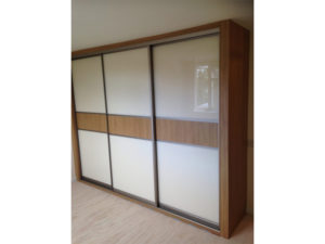 A modern sliding wardrobe with a wooden frame and frosted glass panels. The design features horizontal wooden strips across the center of the doors, adding a contrasting element to the frosted surface. The wardrobe is positioned in a bright room.